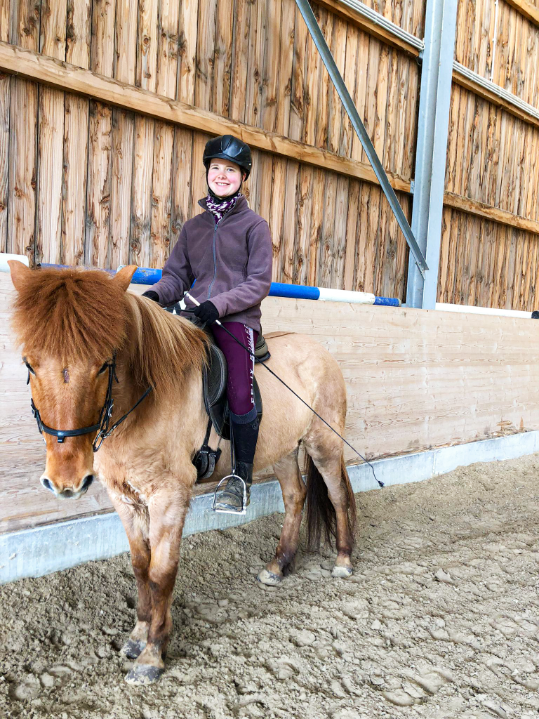 Reiterin mit Helm sitzt lächelnd auf einem Islandpferd in der Reithalle.